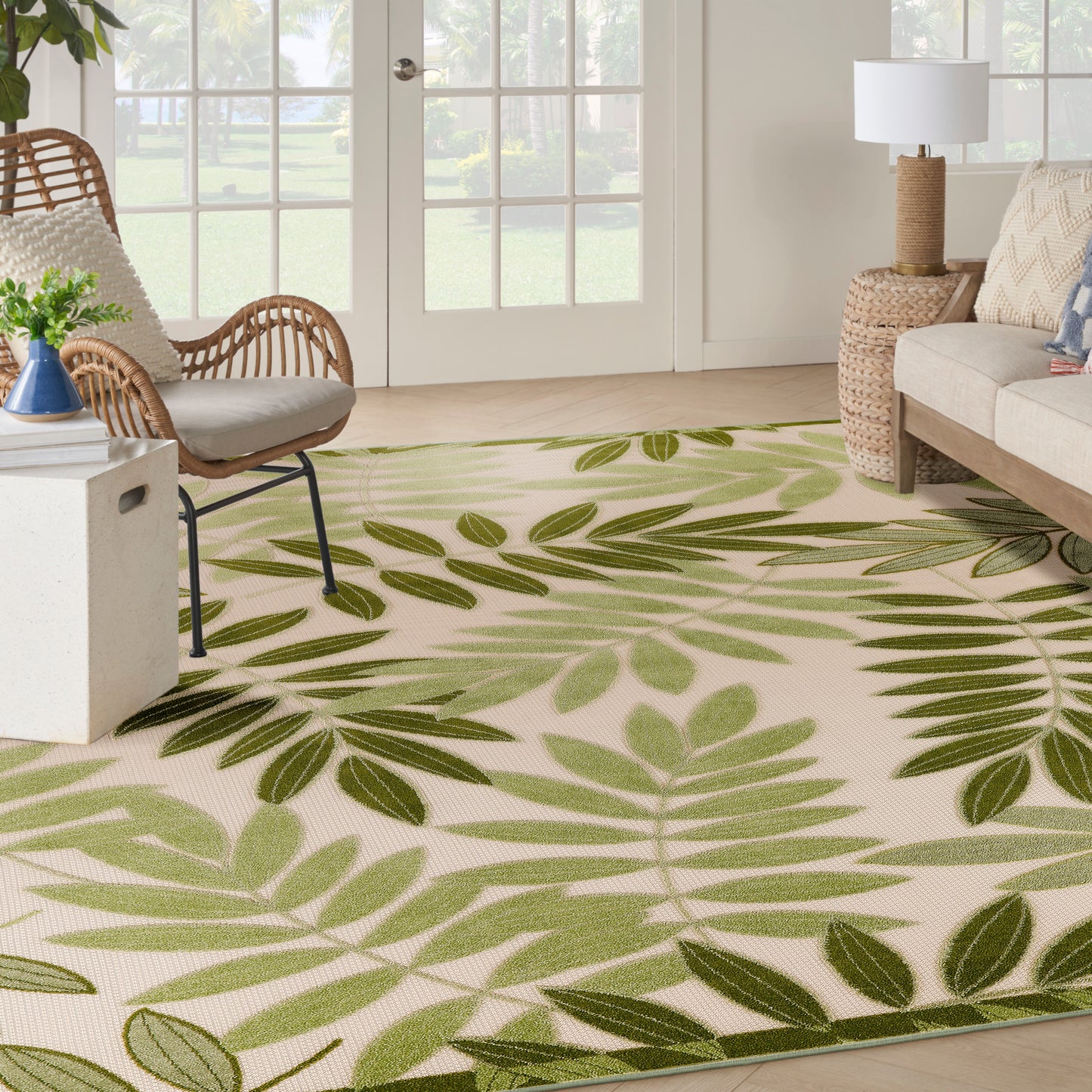Beige outdoor rug 8' x 11' with a large green palm leaf pattern; tropical patio scene with a wicker chair.