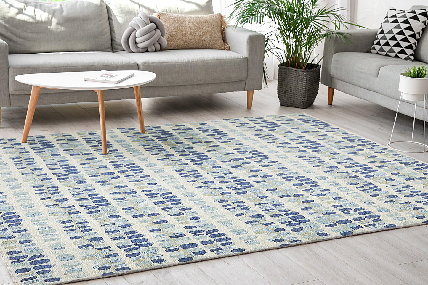 Light beige area rug, 2' x 3', with a blue oval pattern on a light wood floor in a modern living room with a gray sofa.