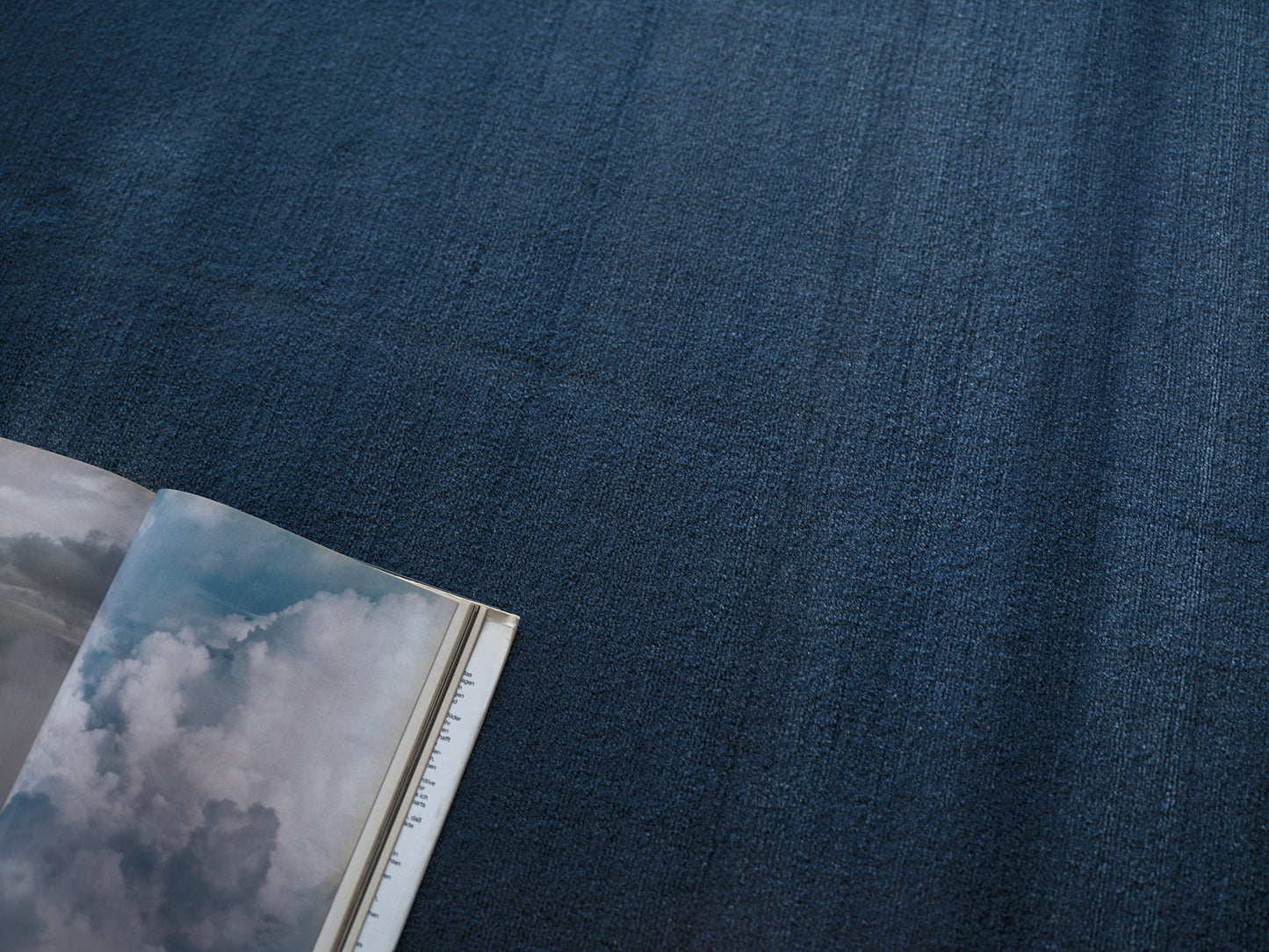 Indigo rug with an open magazine showing a cloudy sky photograph.