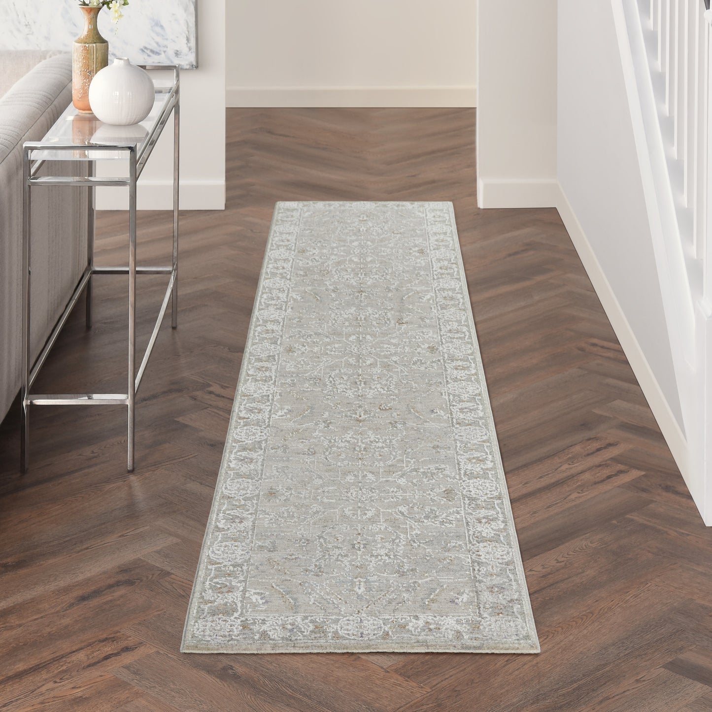 Light gray patterned 10' runner rug on a dark herringbone hallway floor, with a chrome glass-top console table nearby.