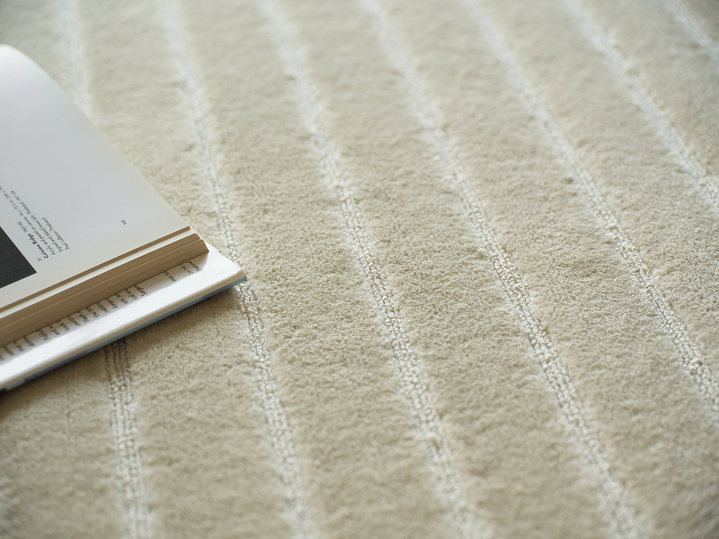 Beige striped textured rug with soft pile; open magazine resting on left edge, cozy home scene.