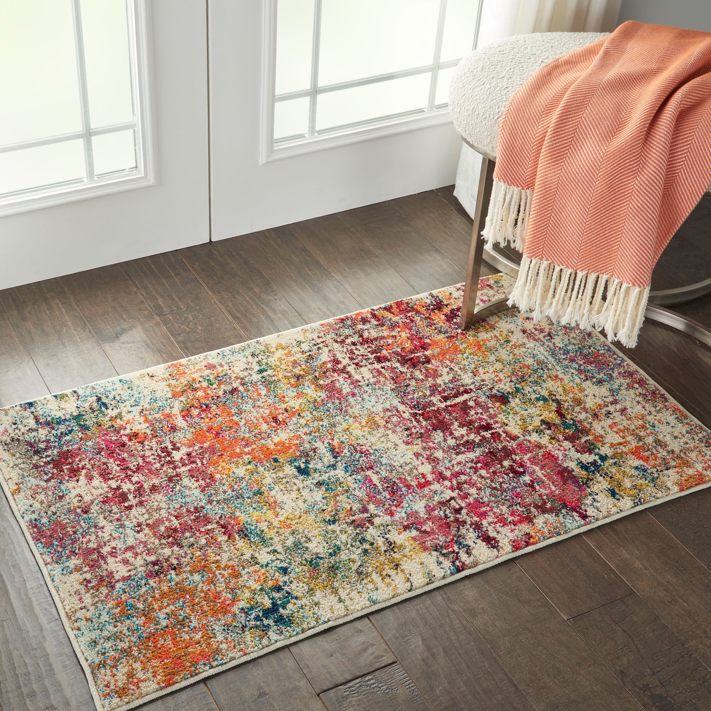 Rectangular multicolor abstract area rug on dark wood floor beside a chair with an orange throw.