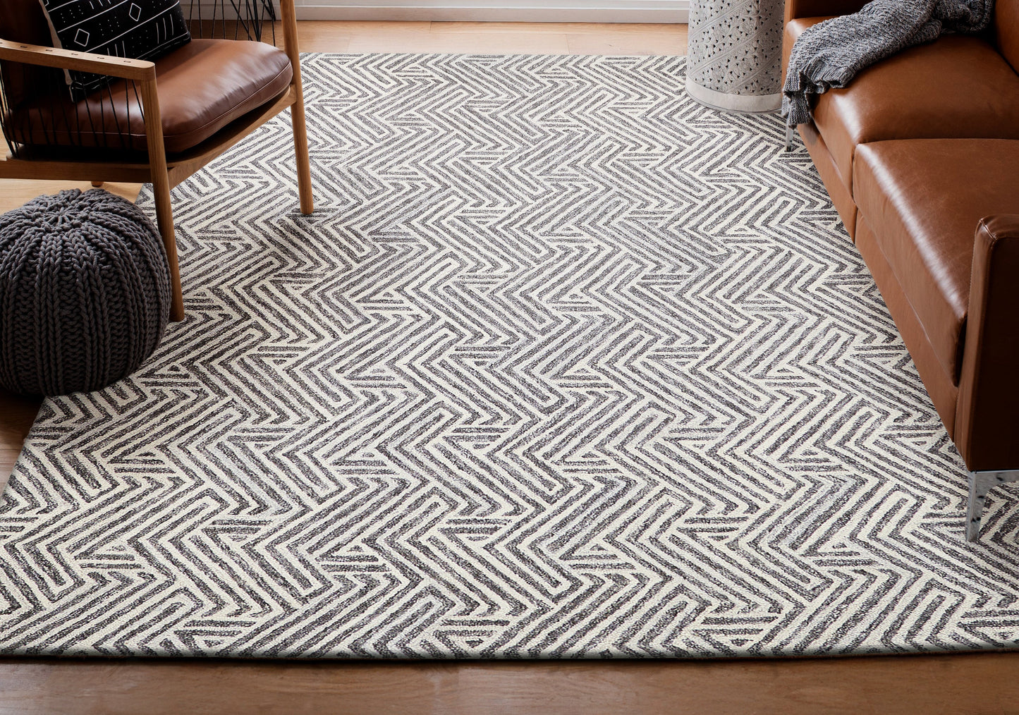 Grey chevron rug with a geometric zigzag pattern in a cozy living room with brown leather sofa, chair and knitted pouf.
