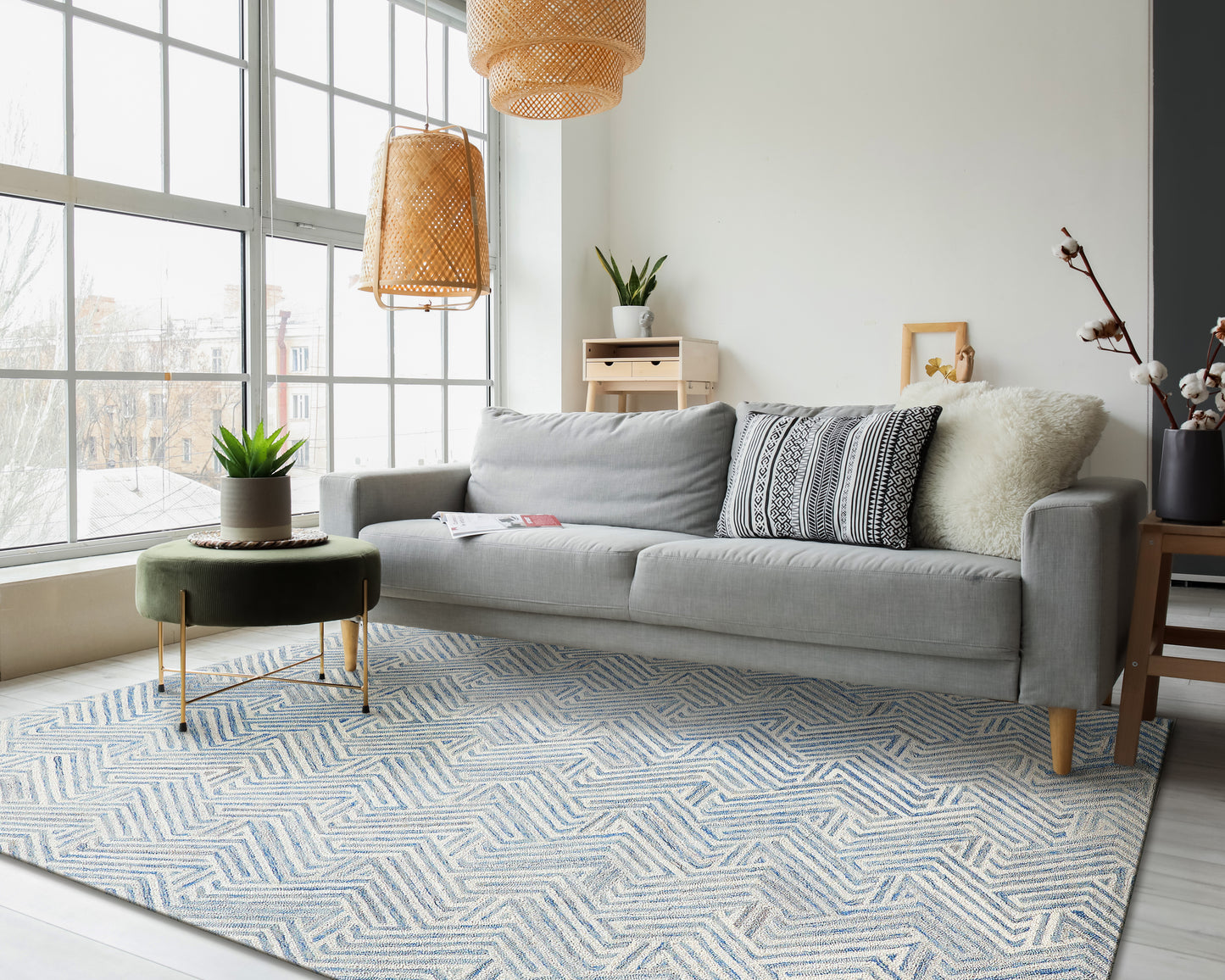 Light gray sofa with patterned cushions in a bright living room; blue chevron rug, wicker pendant lights, and greenery.