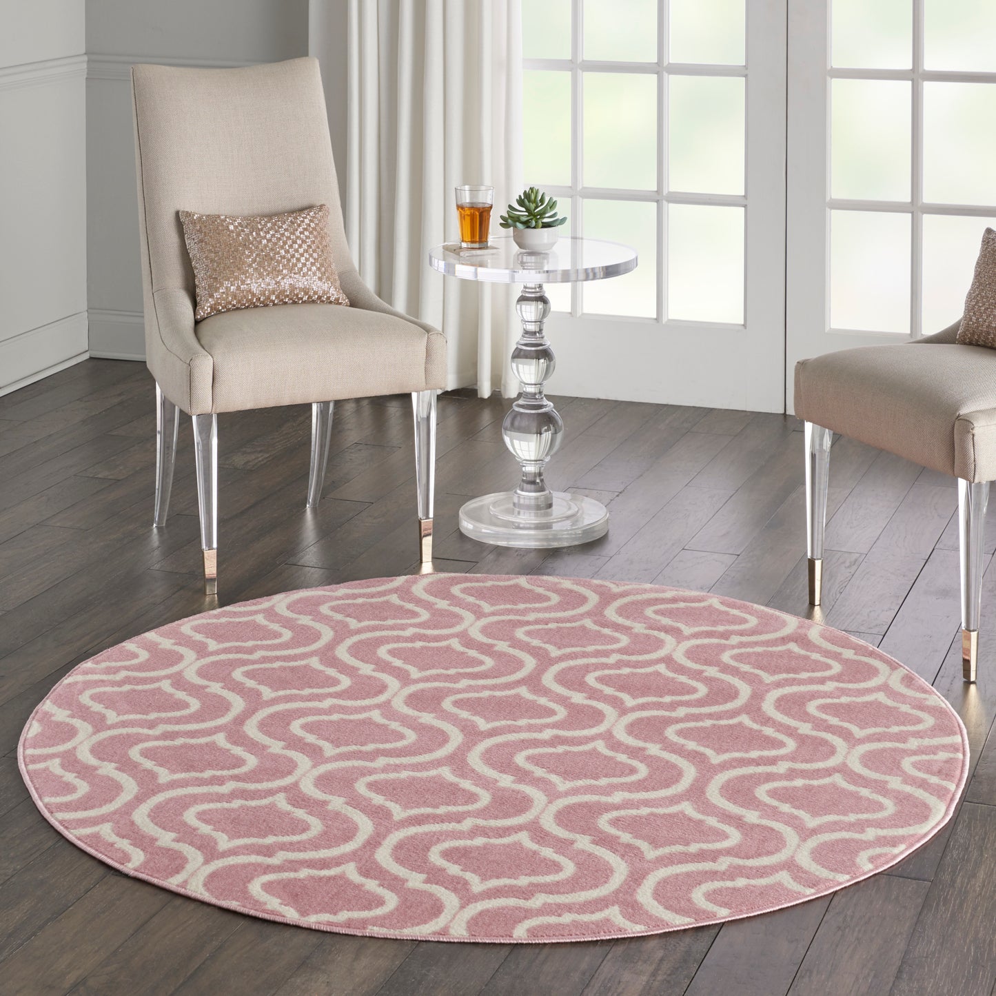 Round pink rug with white loop pattern, beige upholstered chairs with metal legs, glass side table with plant and drink.