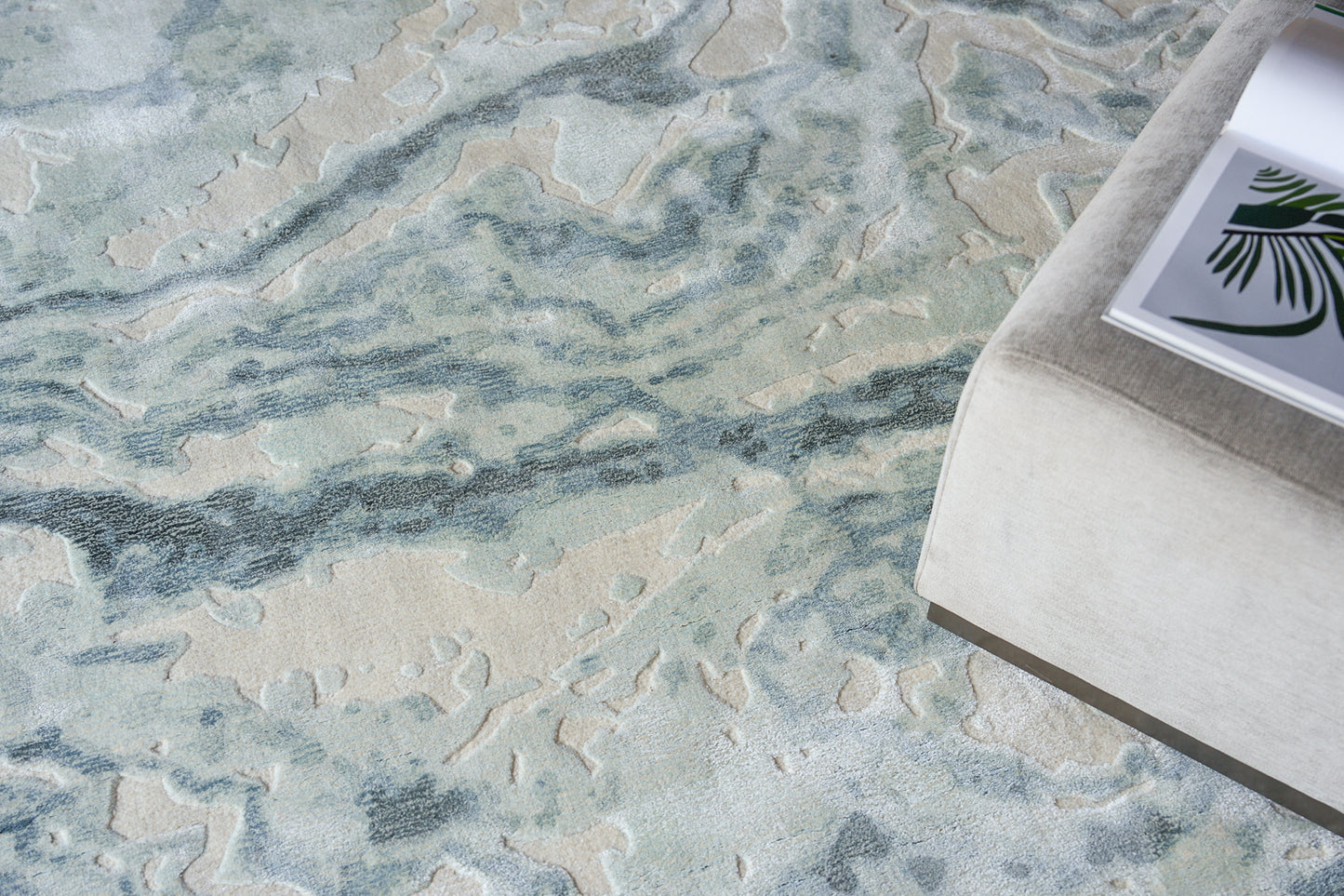 Abstract blue and beige area rug with soft pile; coastal modern style, beside a light gray ottoman with a magazine.