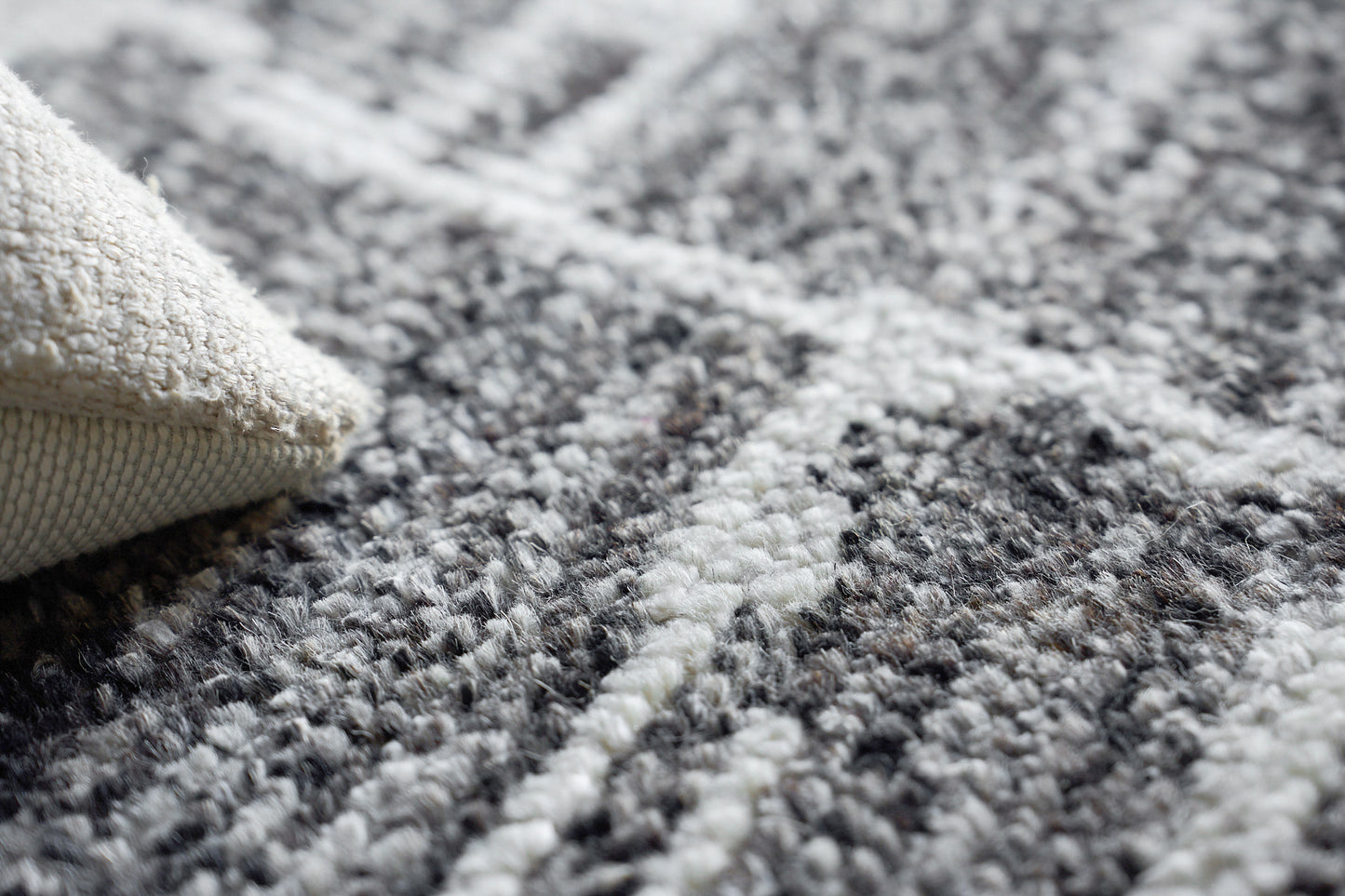 Close-up of a hand-knotted indoor rug in gray, black and ivory with a beige backing.