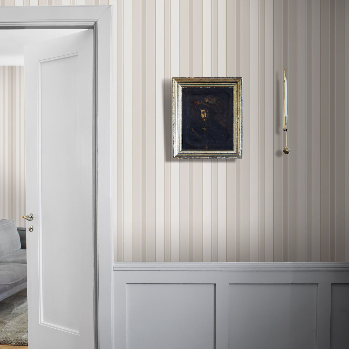 Beige vertical striped wallpaper with white wainscoting, silver-framed dark portrait, white door on the left, brass candle sconce.
