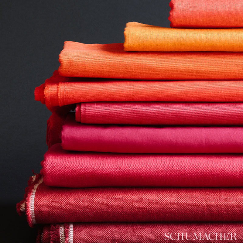 Stack of folded warm-toned fabrics from orange to pink with a textured woven weave and frayed edges against a dark background.