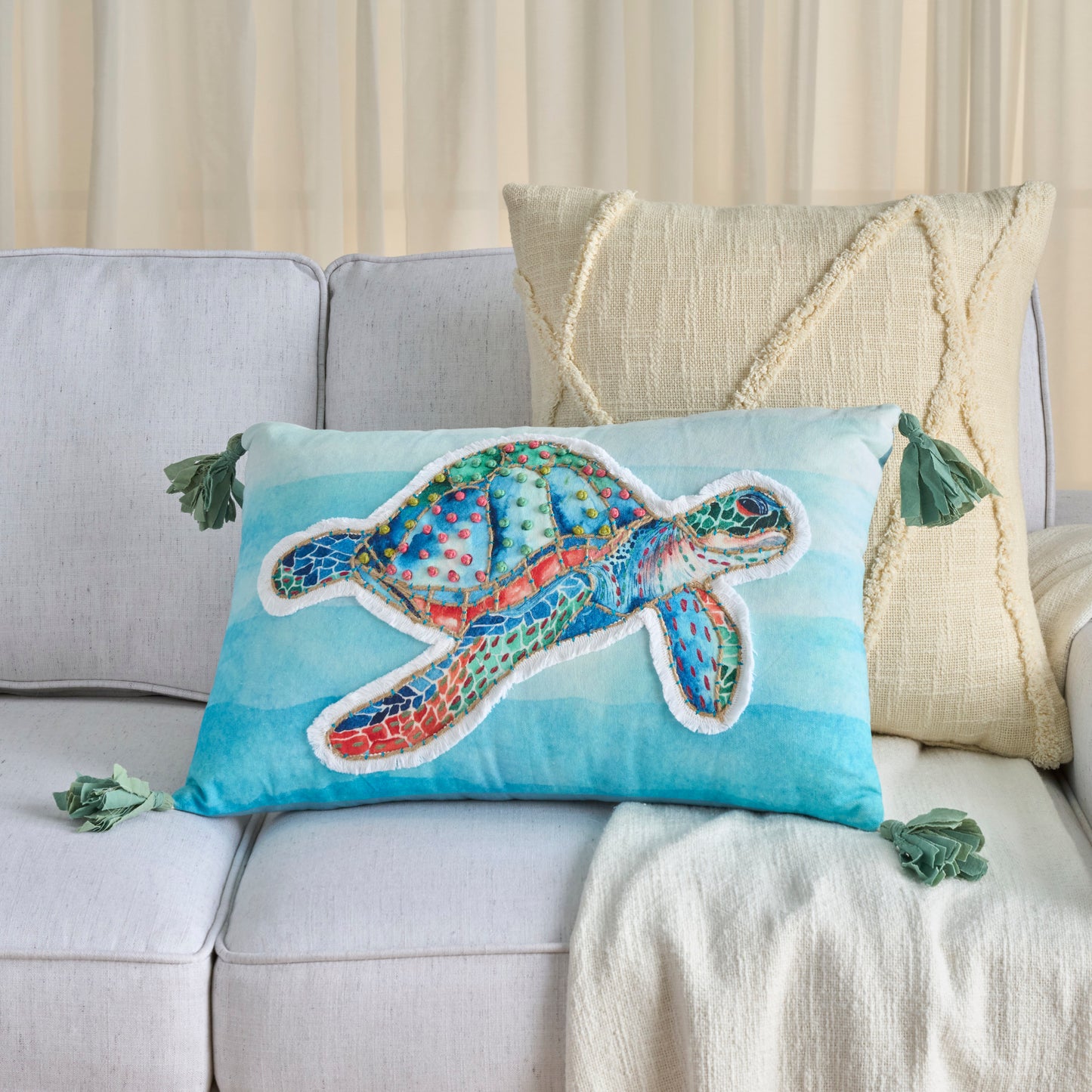 Turquoise rectangular throw pillow with a multicolor sea turtle applique, white outline, green tassel corners, coastal decor.