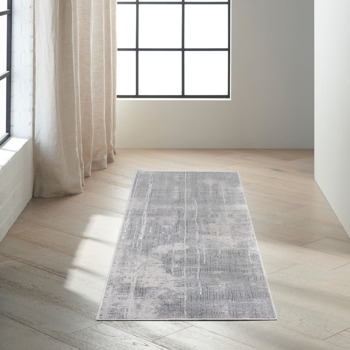 Rectangular gray-blue distressed rug on light wood floor beside beige curtains and a large grid window.