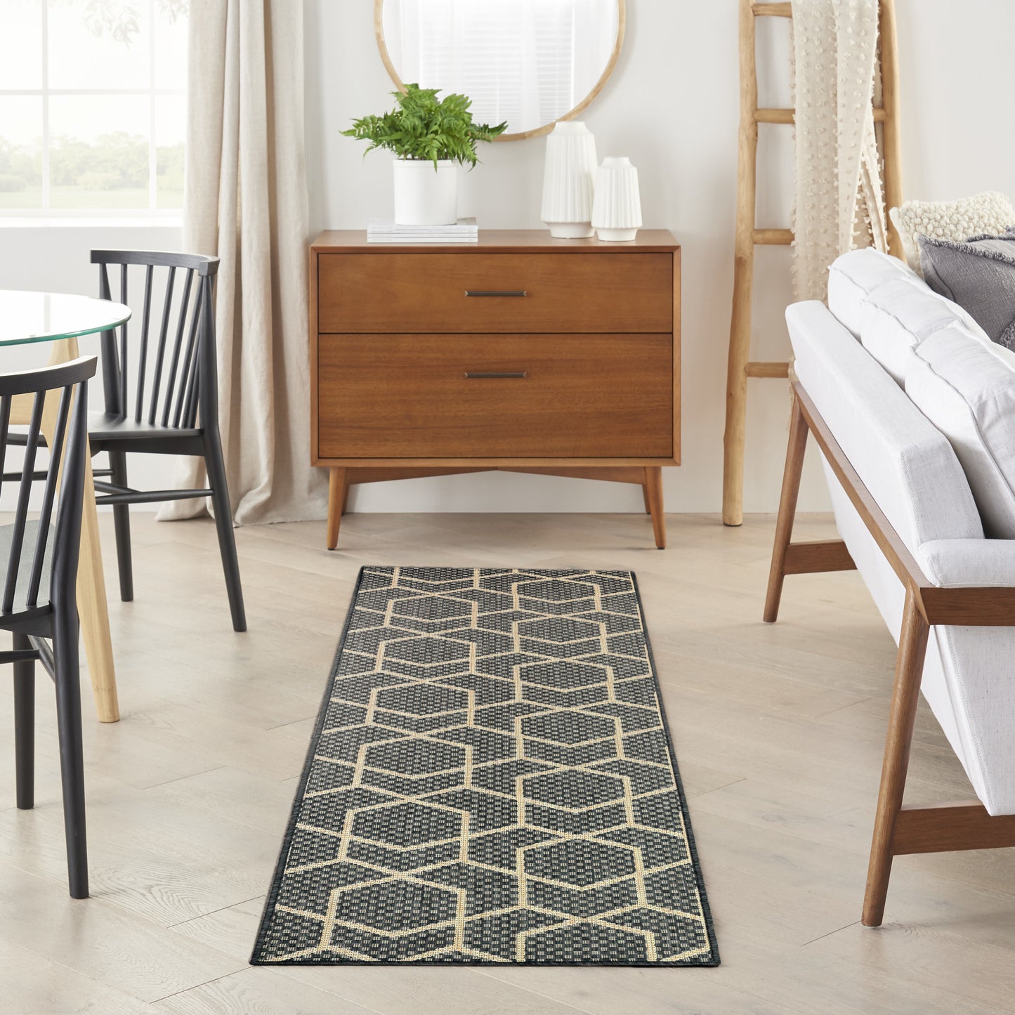 Long geometric hexagon rug runner in black and beige on light wood floor, with mid-century dresser and neutral sofa.