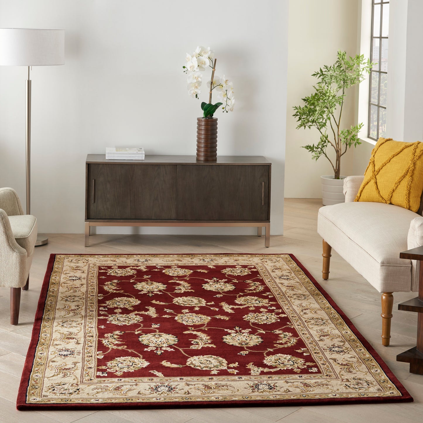 Rust-red oriental rug with ivory floral border in a modern living room; dark wood sideboard, beige seating, yellow cushion.
