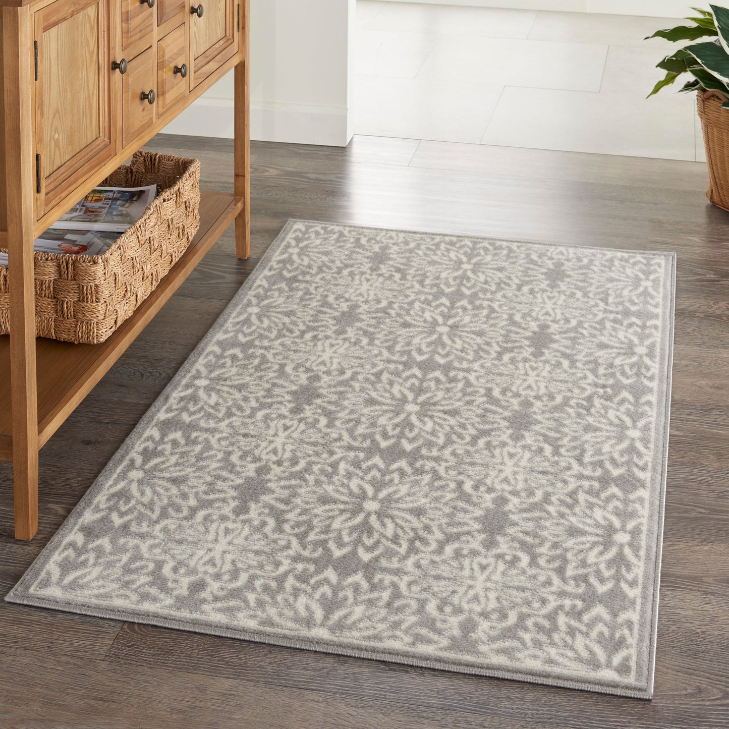 Rectangular grey and ivory damask-pattern area rug on dark wood floor beside a wooden console with a woven basket.