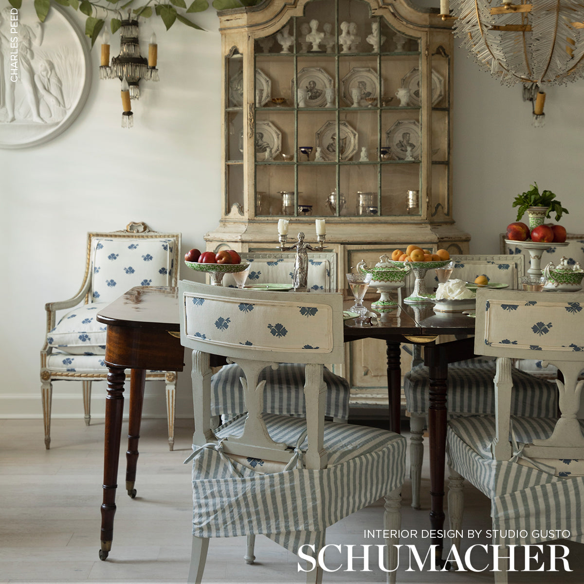 Shabby chic dining set: distressed white chairs with blue floral panels and striped seats, dark wood table, vintage cabinet.