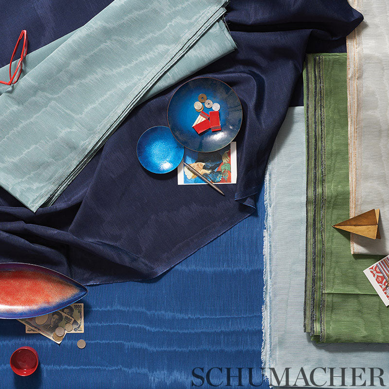 Stacked fabric swatches in navy, teal, light blue and green with a blue plate, postcard, tiny paper boat and red glasses.