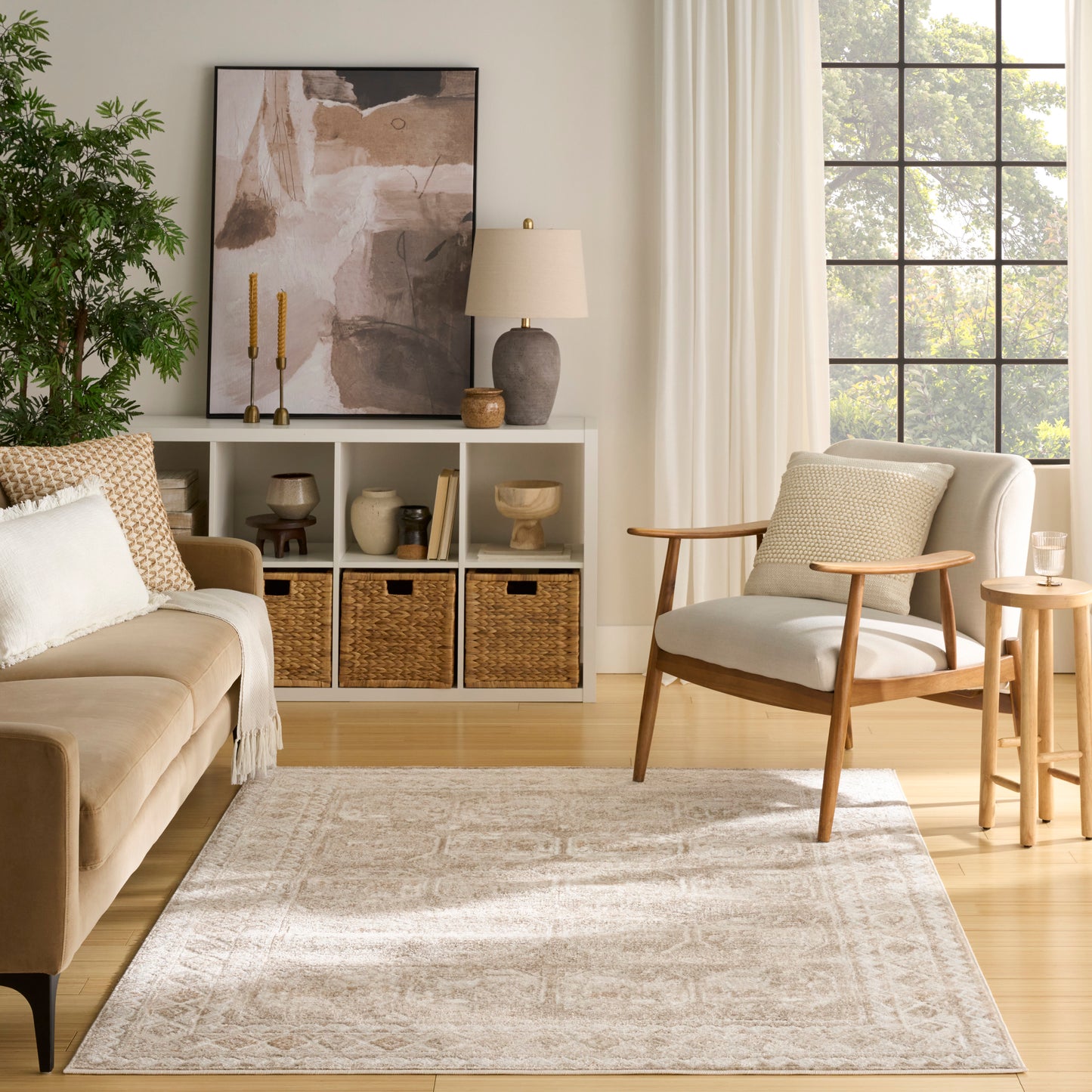 Neutral living room featuring a vintage 5' x 7' rug, beige sofa, light wood lounge chair, woven baskets, plant, and sunlit window.