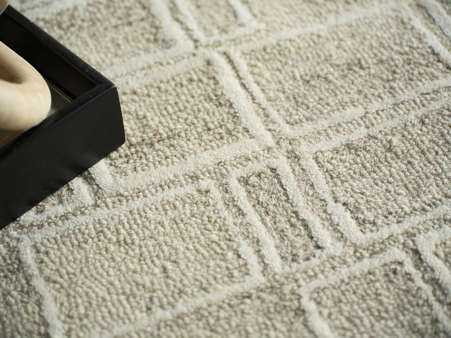 Beige textured geometric rug with a black rectangular box on it and a partial bare foot visible inside the box.