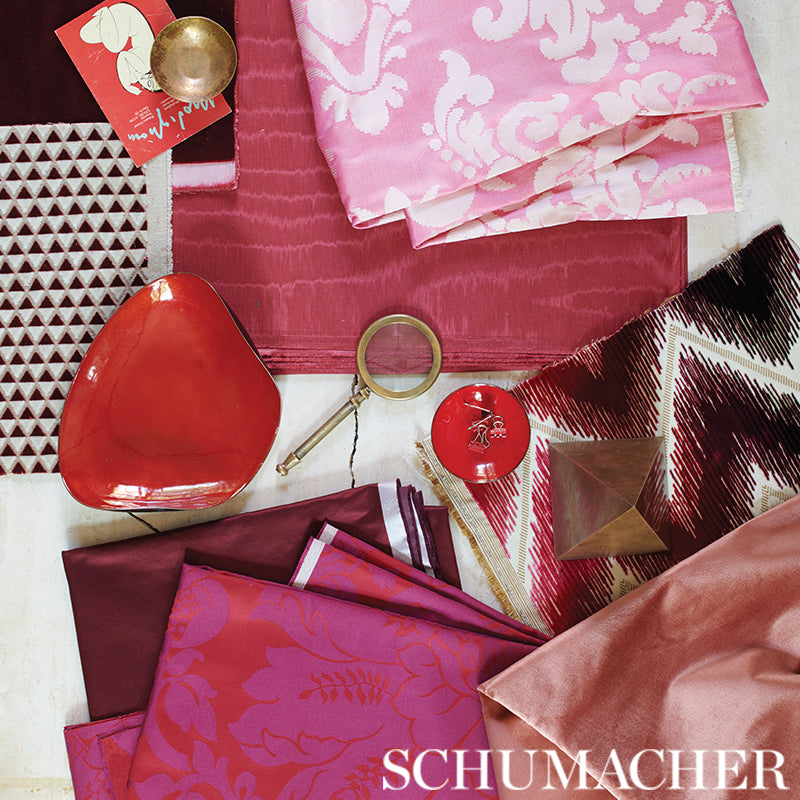 Pink, burgundy and red satin fabric swatches with a red glass bowl, brass ring and candle.