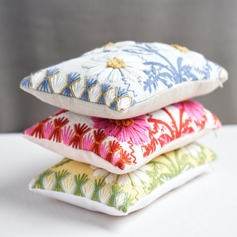 Stack of three square embroidered cushions with floral motifs in blue, pink and green.