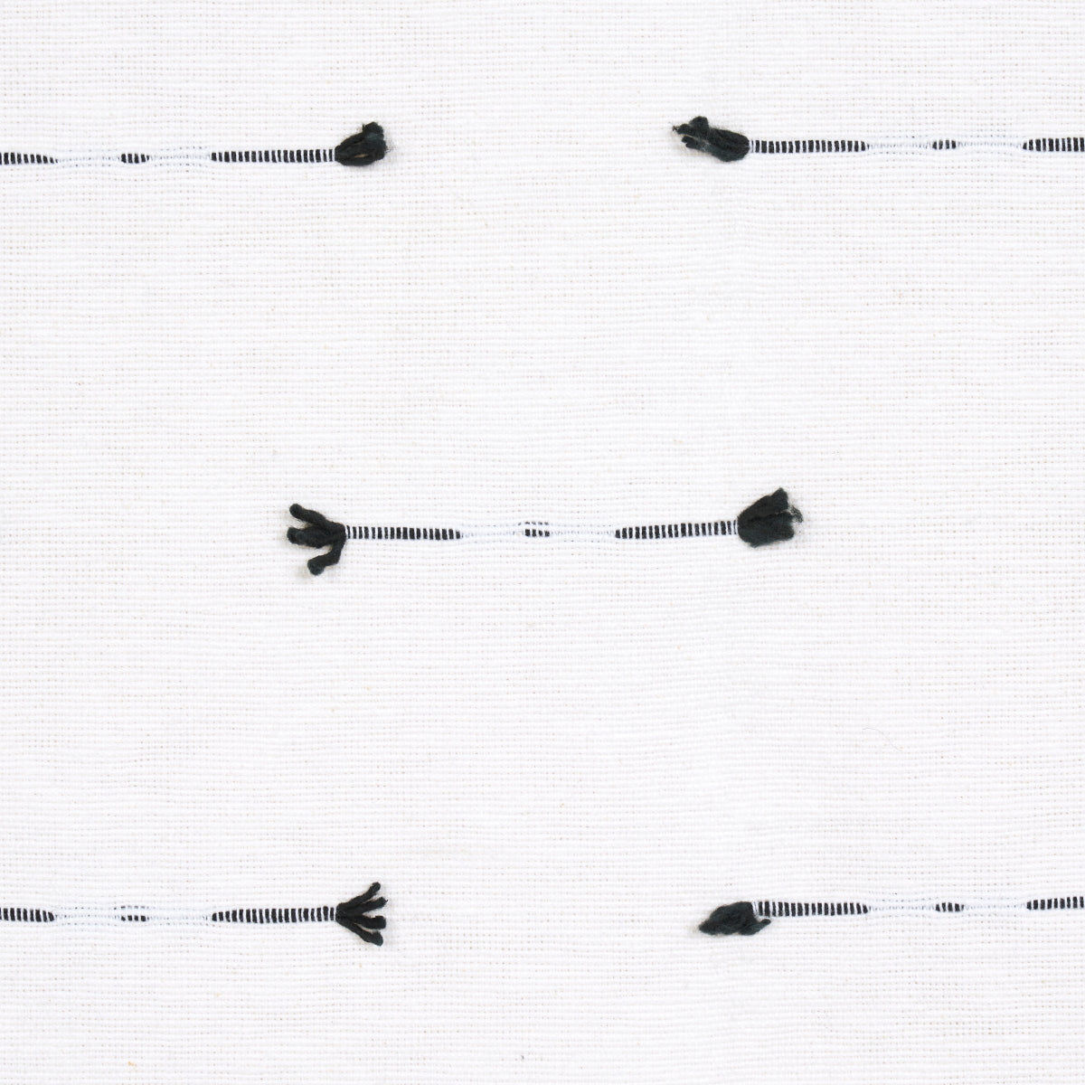 White fabric swatch with black-striped tassel trim cords laid horizontally; small black tassels at ends.