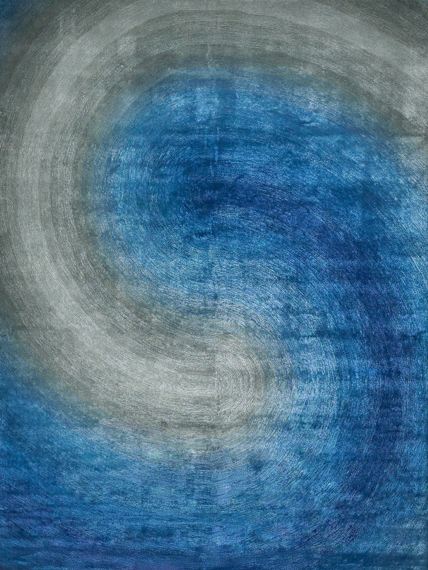 Abstract circular ripple rug in blue and gray tones with textured fibers; indoor hand-tufted.
