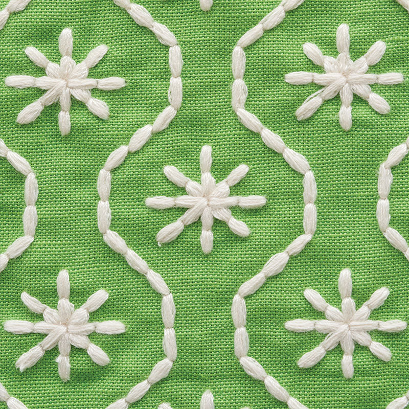 Green fabric with white embroidered chain-loop motifs and starburst flowers.