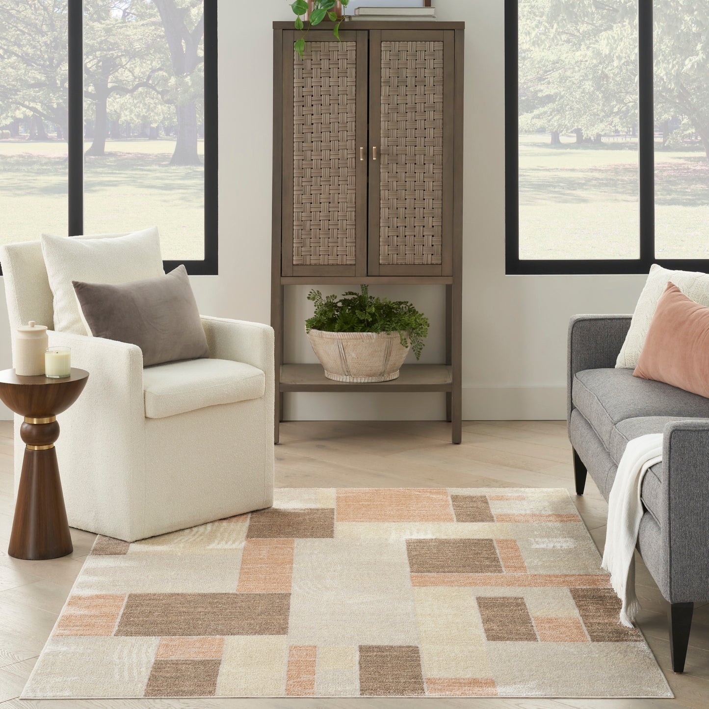 Cozy living room with beige armchair, gray sofa, woven cabinet with lattice doors, plant basket, and a geometric beige-brown rug.
