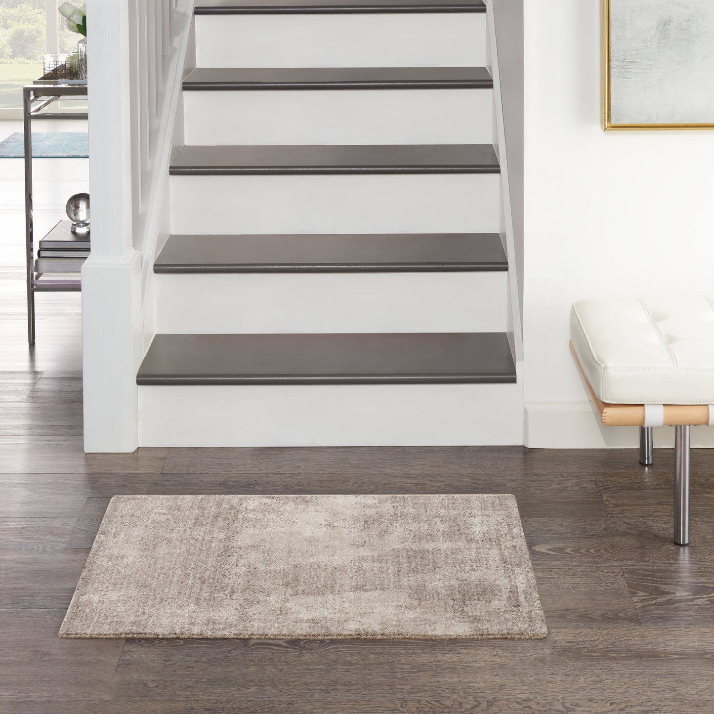 White staircase with dark wood treads, beige rug, modern white bench, framed art in a contemporary entry hall.