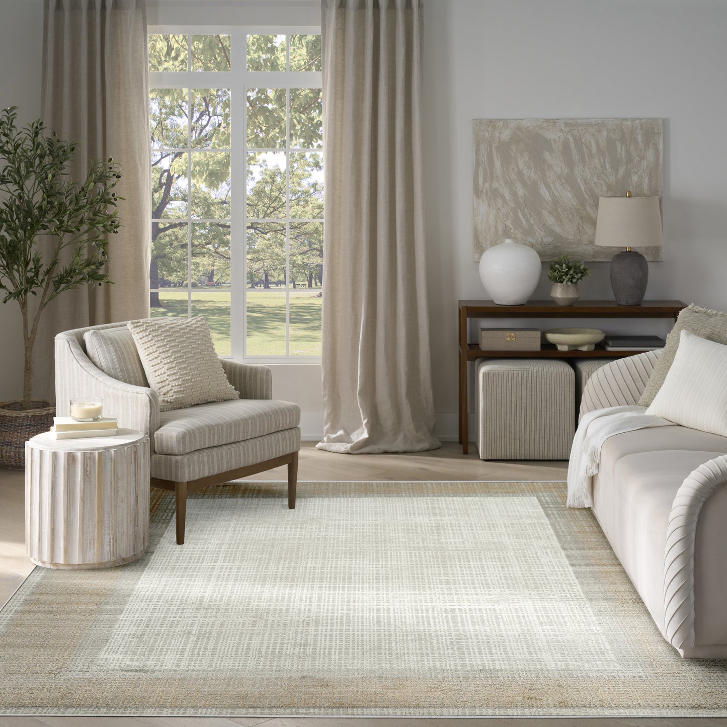 Neutral living room with beige fabric sofa, striped armchair, woven rug, linen curtains, wood console, and green plant.
