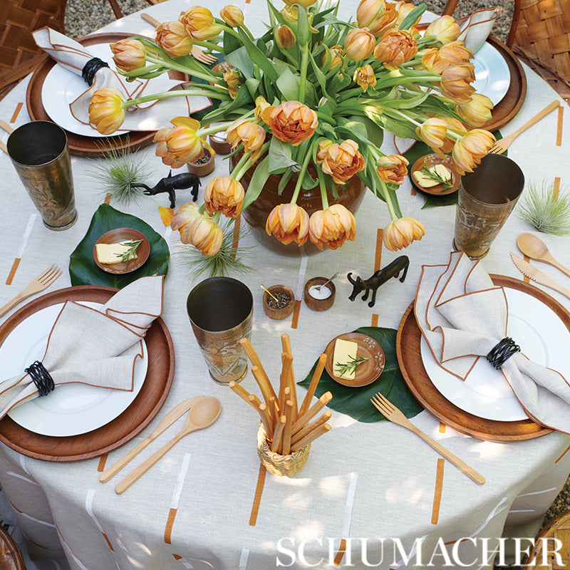 Rustic table setting with orange-yellow tulip centerpiece & brown chargers & white napkins & wooden utensils & brass goblets.
