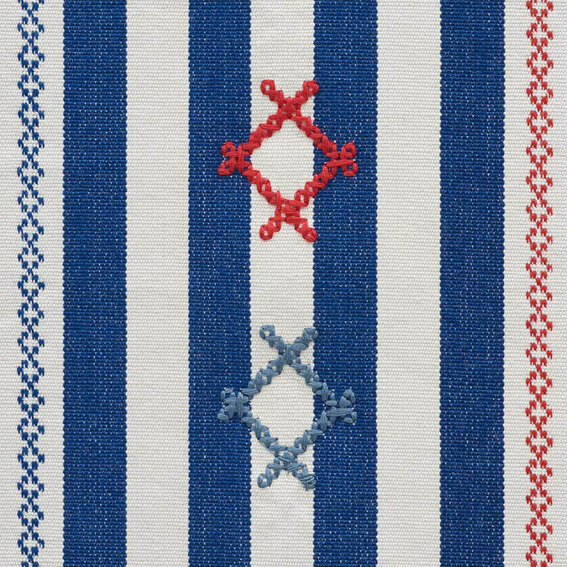 Woven textile with navy blue and white vertical stripes, red and pale blue diamond knot motifs, bordered by zigzag trims.