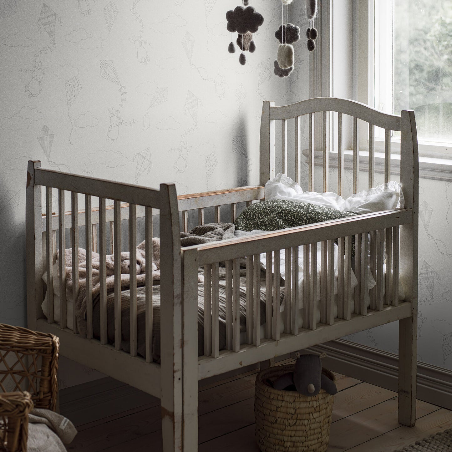 Distressed white wooden baby crib with slatted sides in a cozy nursery, cloud mobile overhead.