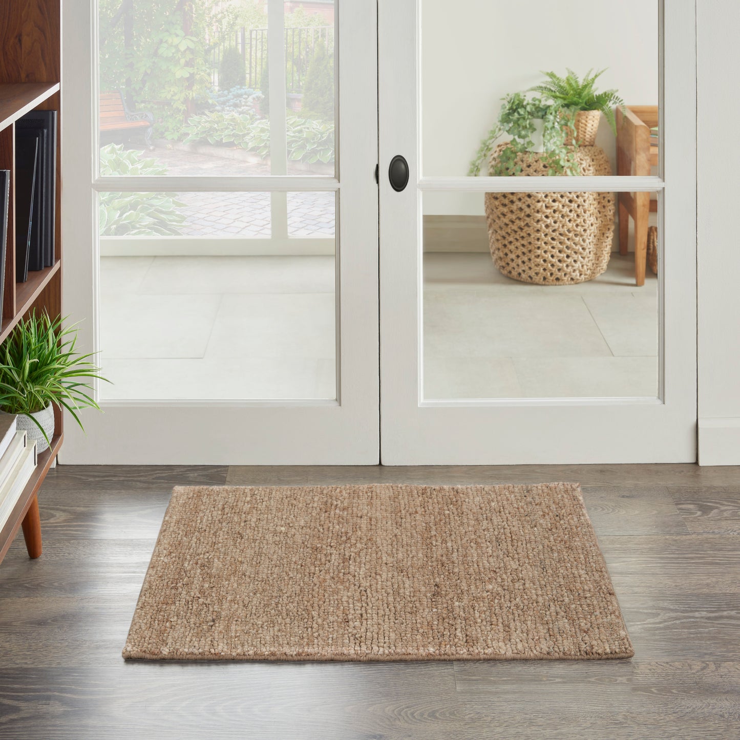 Rectangular natural jute entry rug on dark wood floor in front of white-framed glass French doors; rustic coastal style.