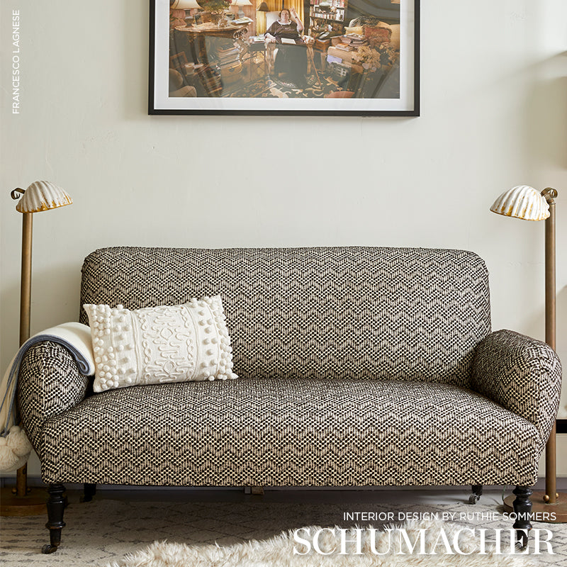 Zigzag beige-brown fabric sofa with dark wood legs, white textured pillow, brass floor lamps on each side.