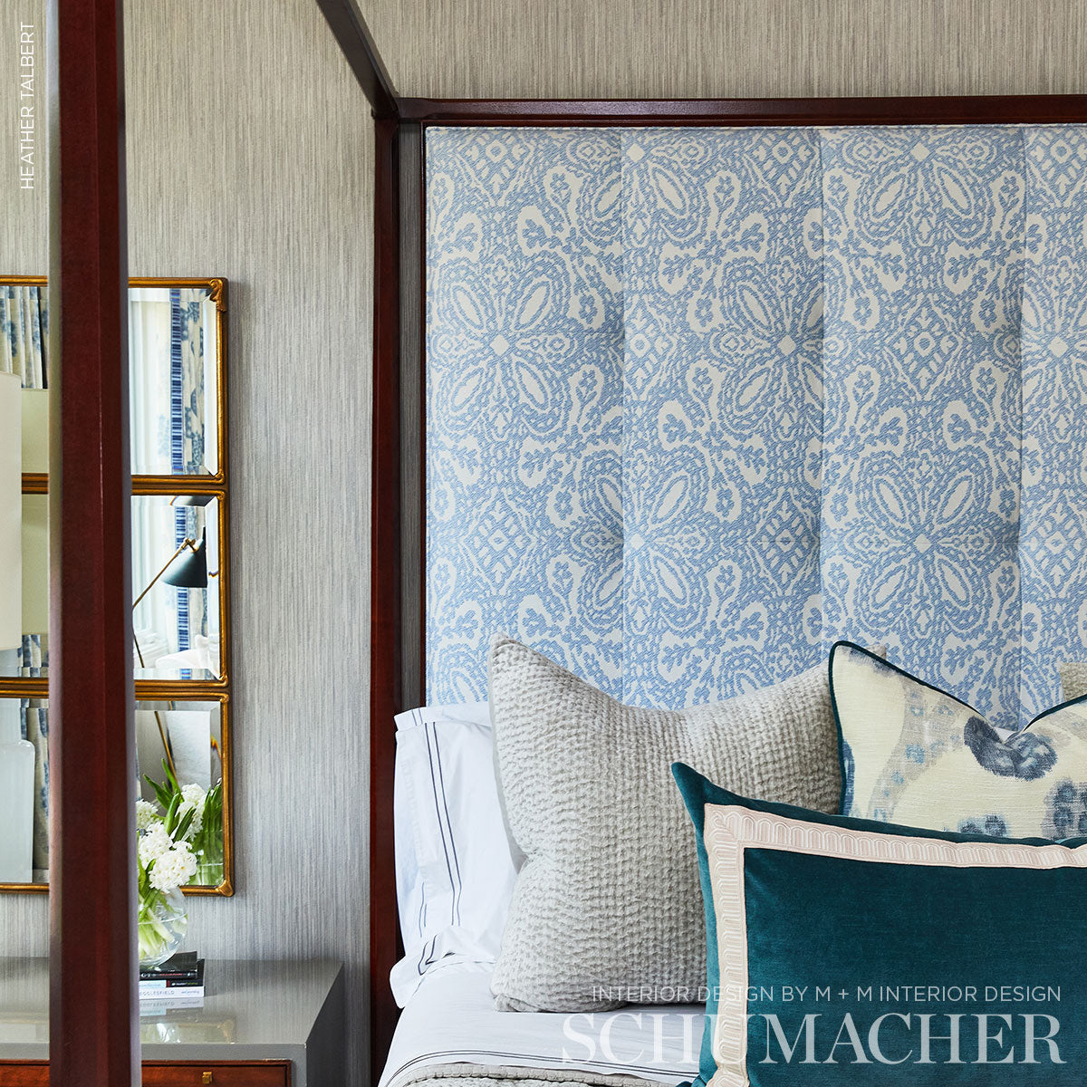 Blue damask-patterned wall panel with a dark wood frame, seen behind a white bed with beige and teal cushions.