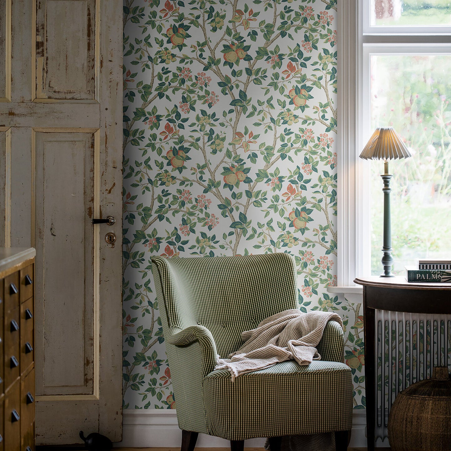 Floral wallpaper pattern with green leaves and orange blossoms; foreground shows a green checkered armchair with a beige throw in a rustic room.