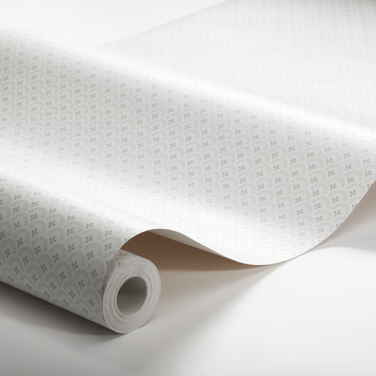 White wallpaper roll with subtle gray floral pattern, partially unrolled with a curved sheet edge.