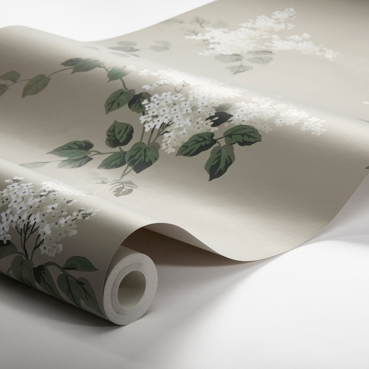 Beige wallpaper with white flowering clusters & green leaves, rolled up on a tube.