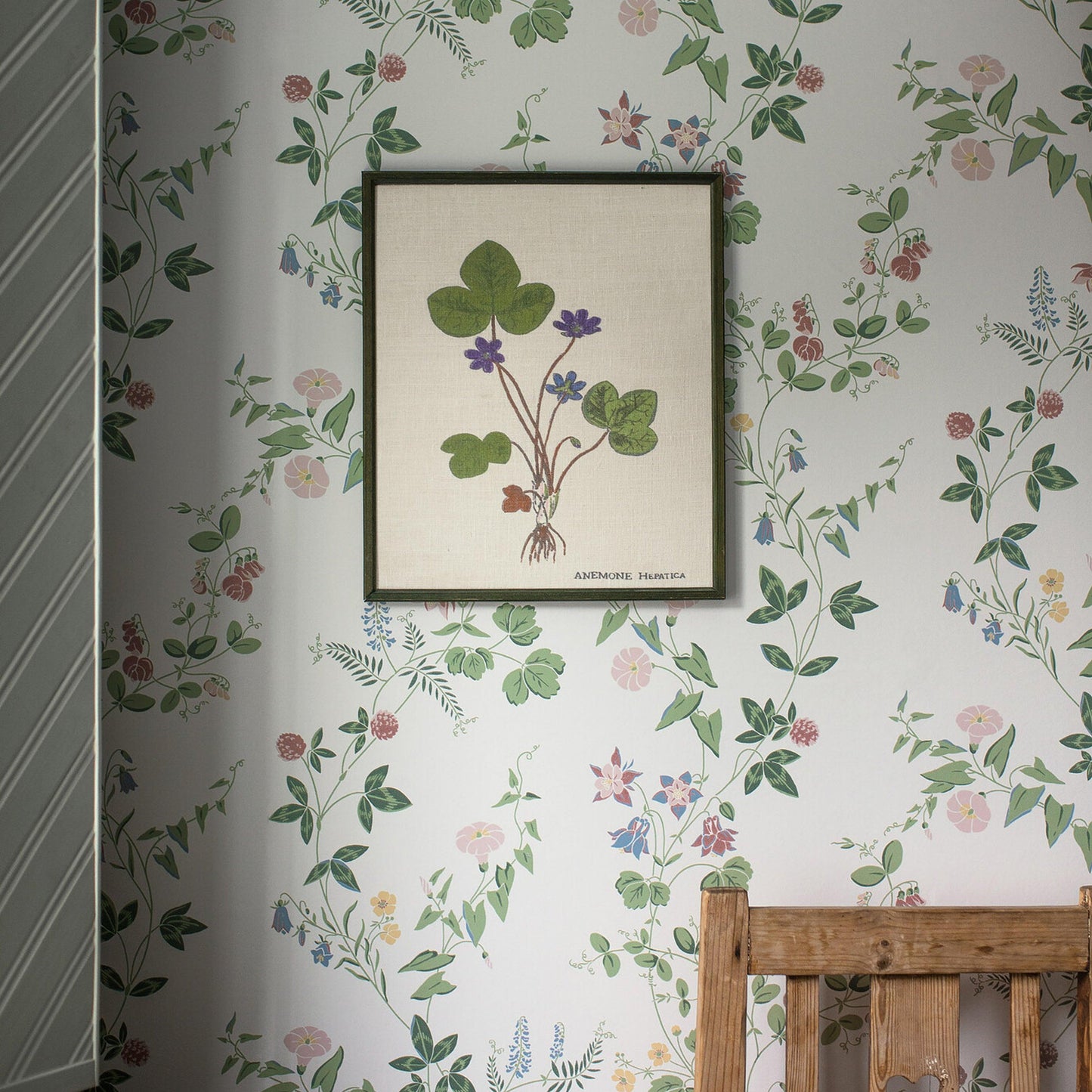 Ivory wallpaper with a hepatica botanical motif in green leaves and purple blooms; bed frame visible nearby.