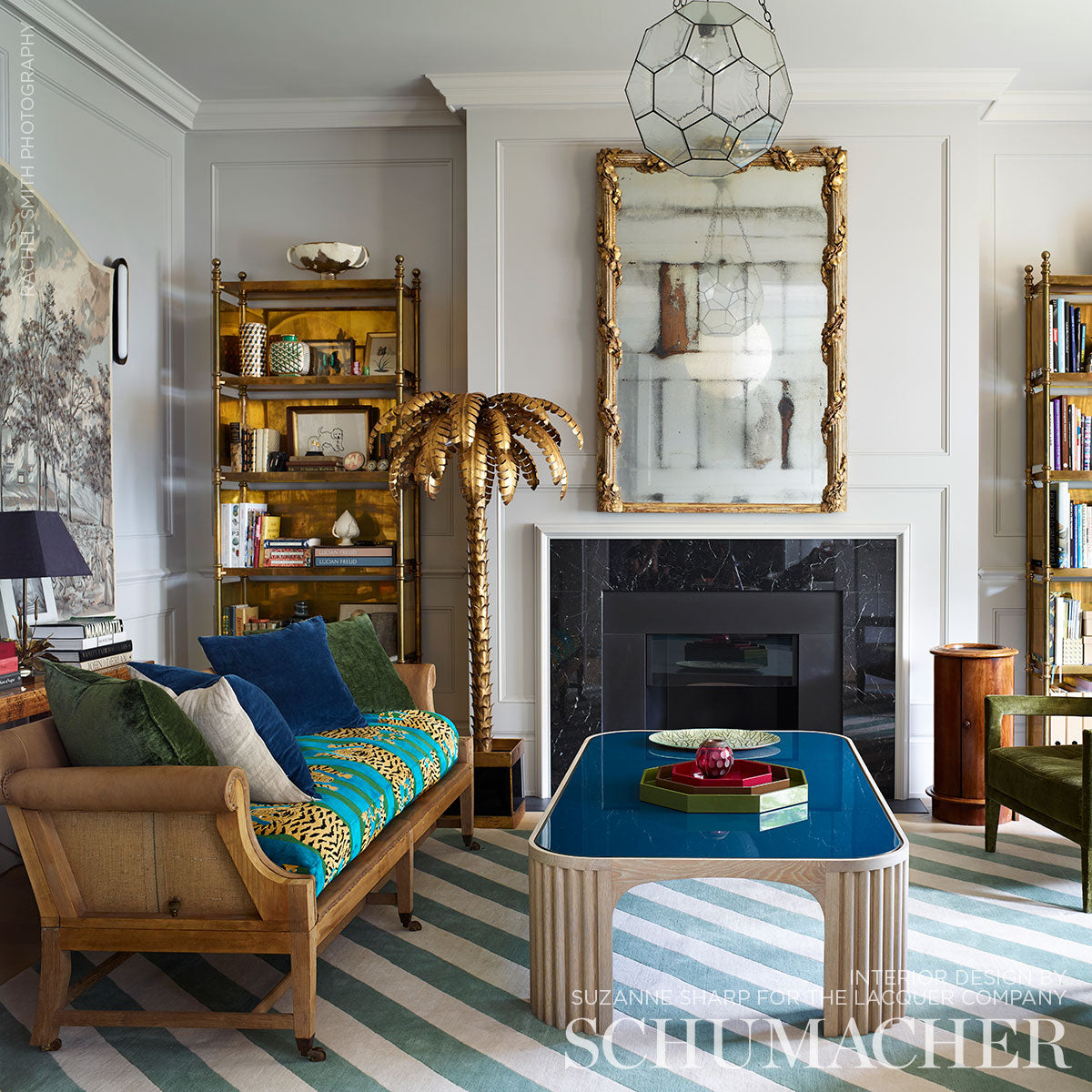 Gold palm tree sculpture beside a blue glass-top coffee table in a gray-paneled living room with striped rug.