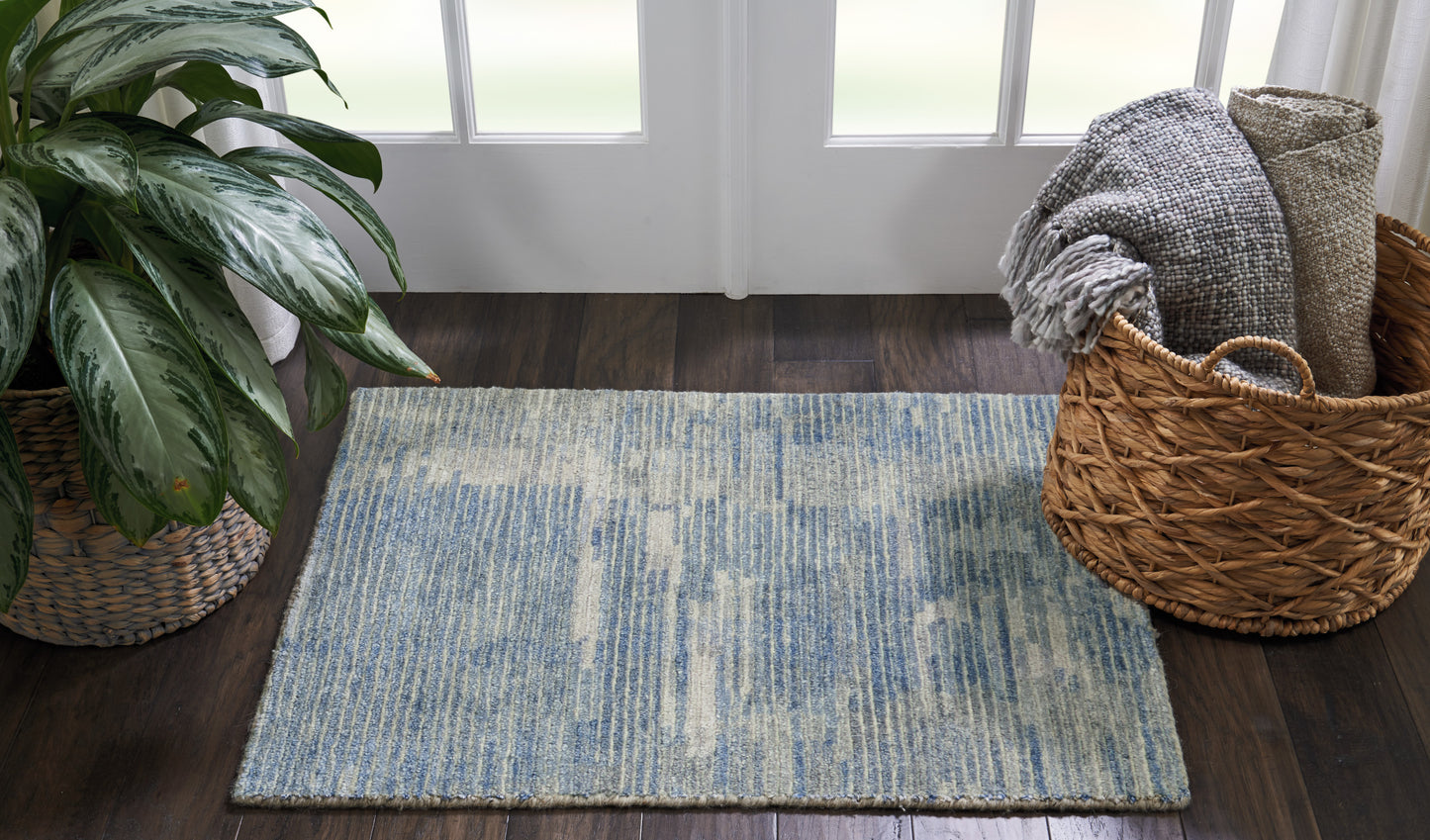 Rectangular blue and cream flat-weave area rug on dark wood floor, with a plant to the left and a woven basket nearby.