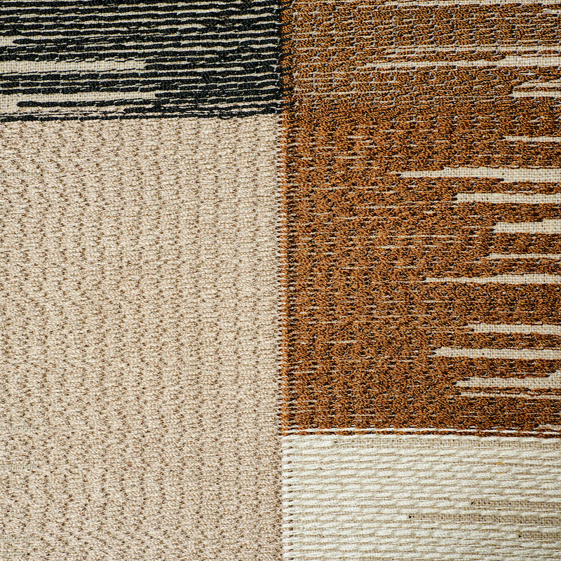 Close-up of a patchwork area rug with beige, tan and brown blocks and textured striped accents.