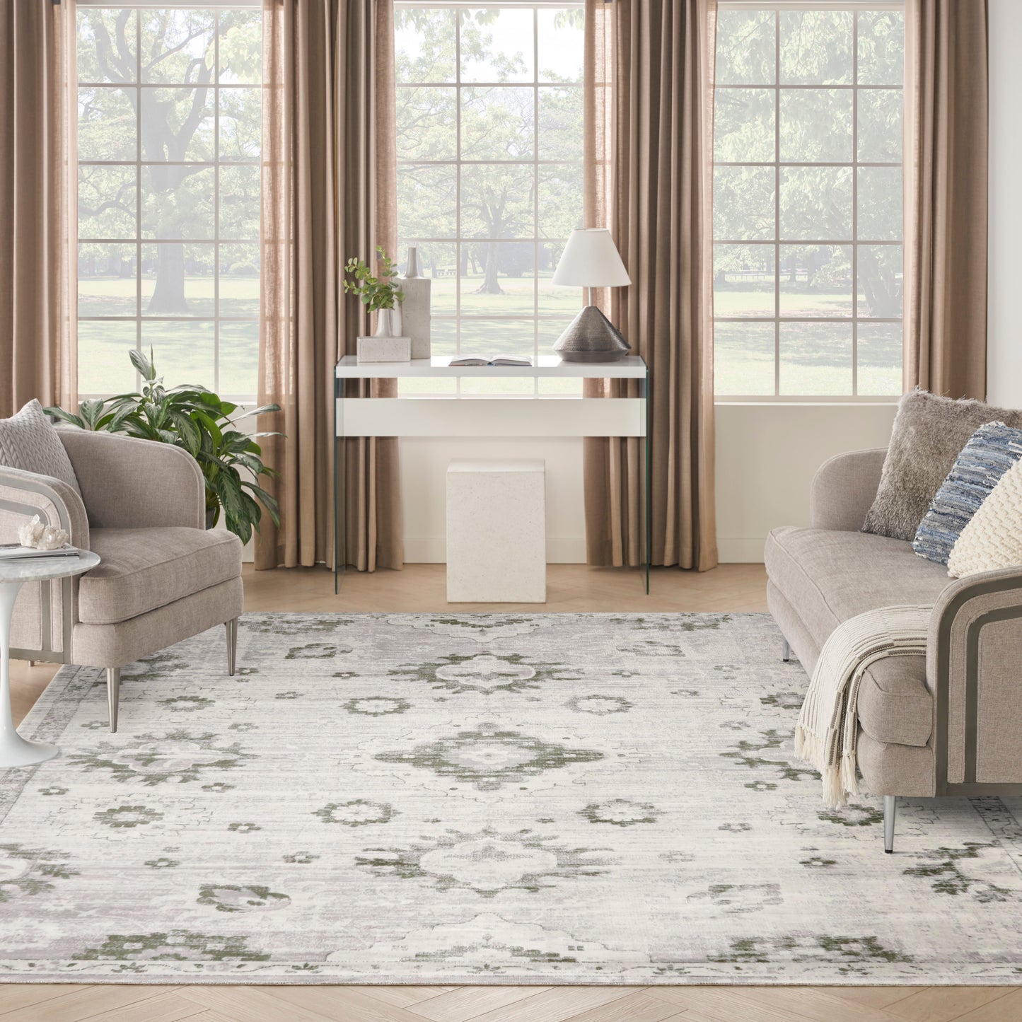 Neutral living room with beige sofas, gray ivory floral rug, white console table, lamp, plant, & tan-curtained windows.