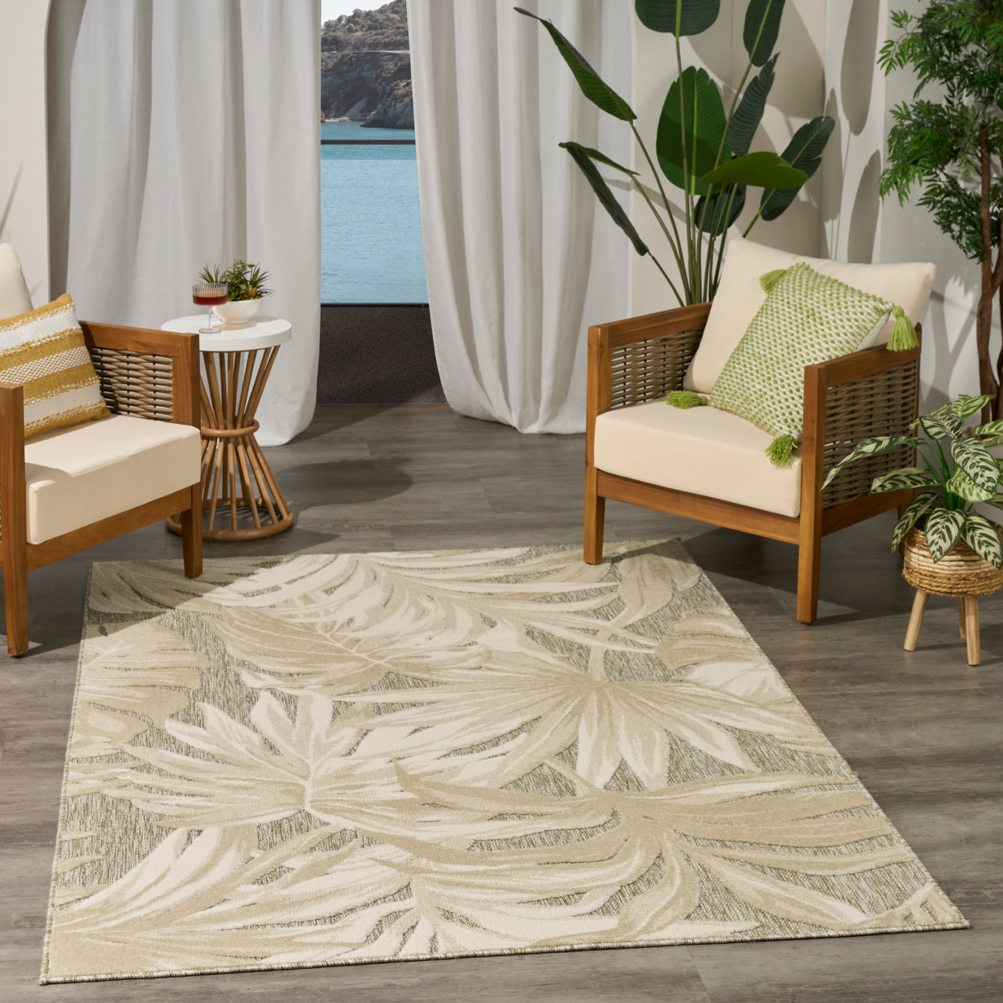 Beige palm-leaf patterned area rug on wood floor; coastal living room with cream cushions & green plants.