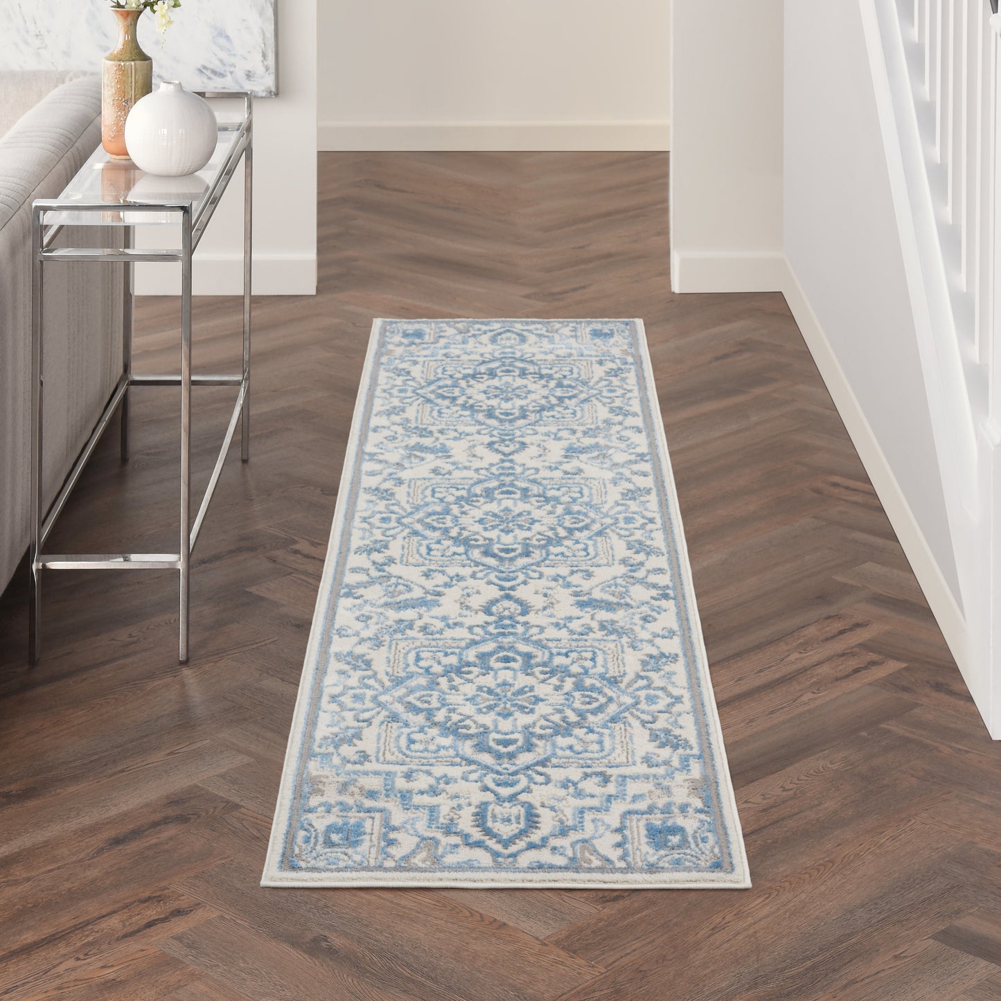 Blue and ivory ornate runner rug with damask medallion pattern and pale border in a hallway on wood flooring.