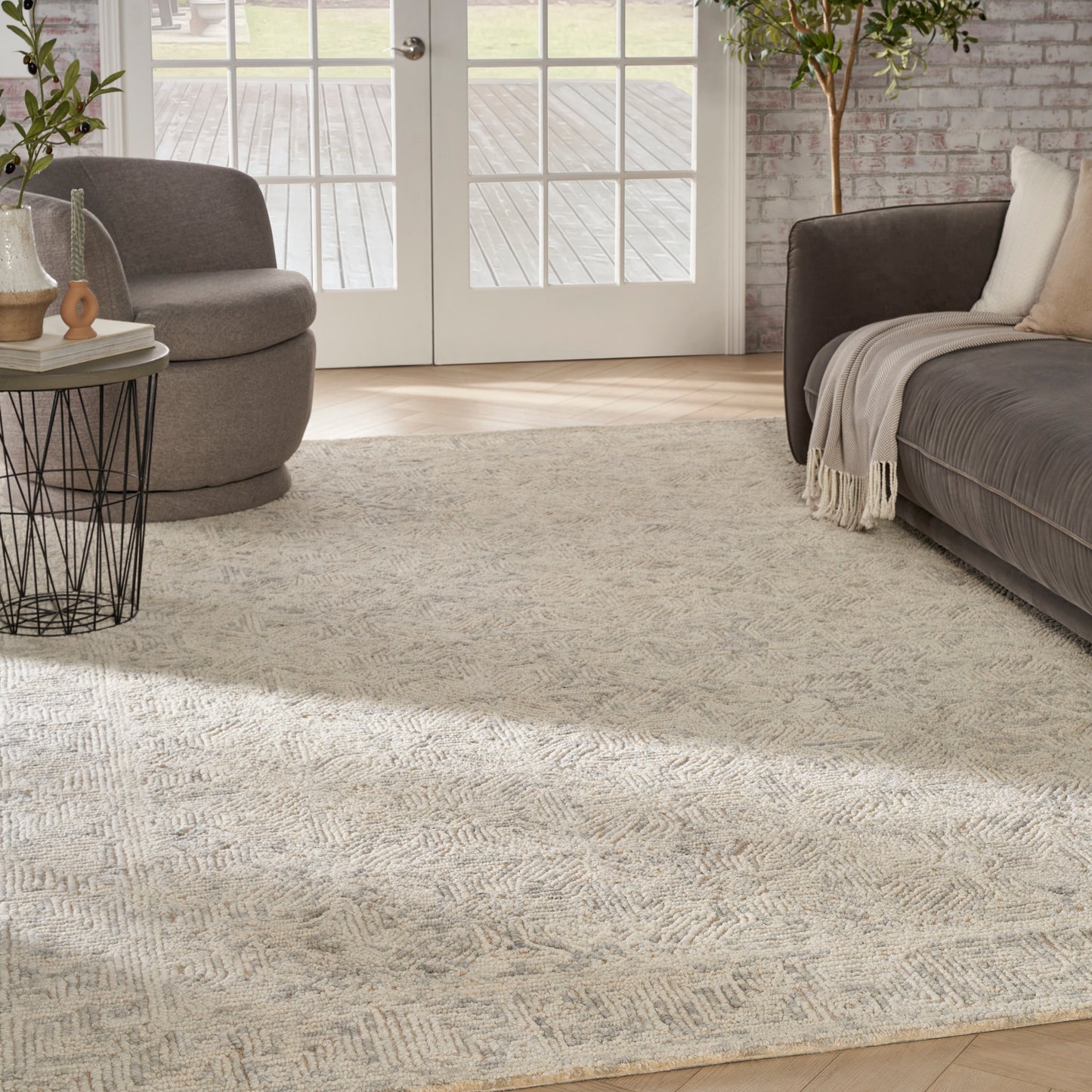 Soft beige woven area rug with a subtle geometric pattern under a gray sofa and round taupe lounge chair.