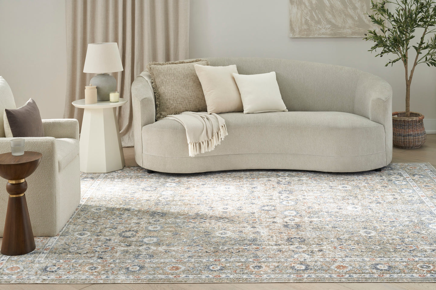 Vintage 7' x 9' rug in light beige with a subtle pattern, shown in a living room with a curved beige sofa, cream armchair, side table, lamp and a potted plant.