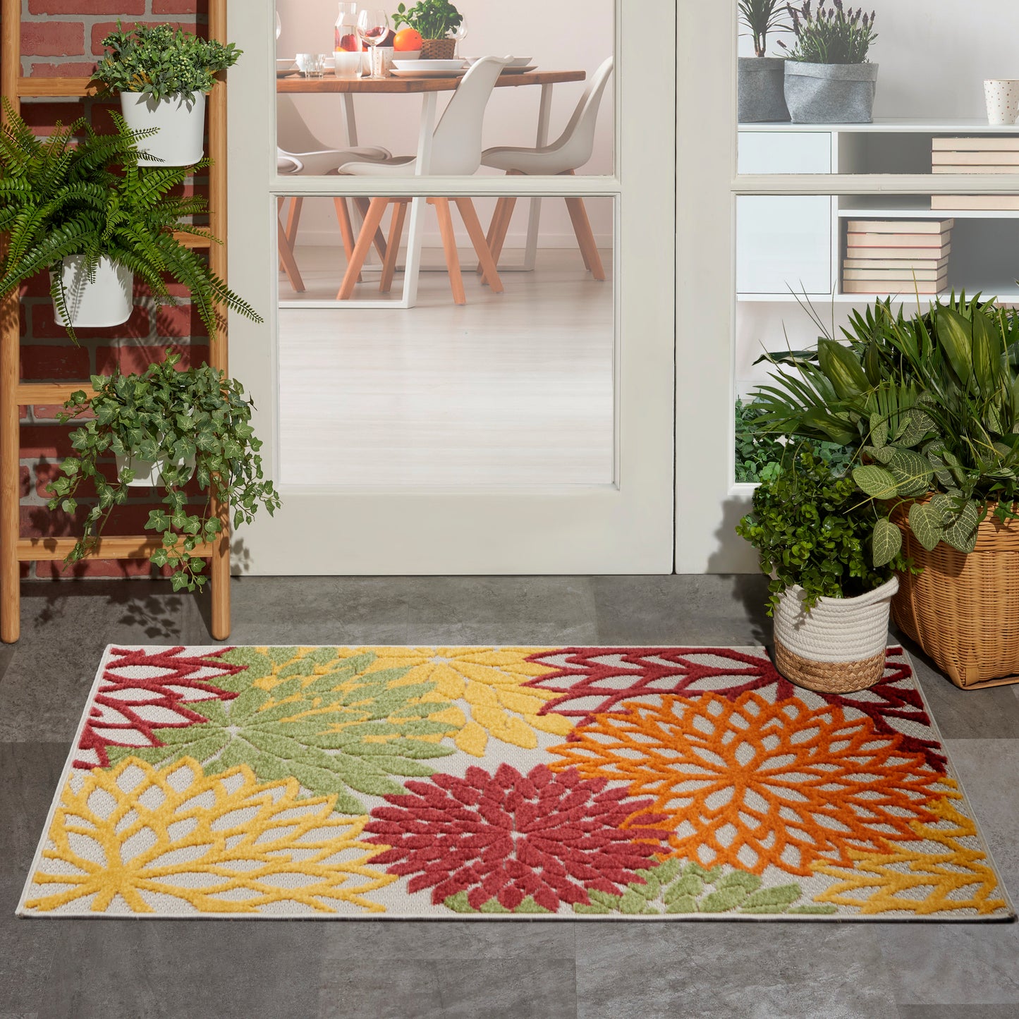 Colorful floral area rug with large yellow, green, red & orange petals, placed at entry with potted plants & glass doors.