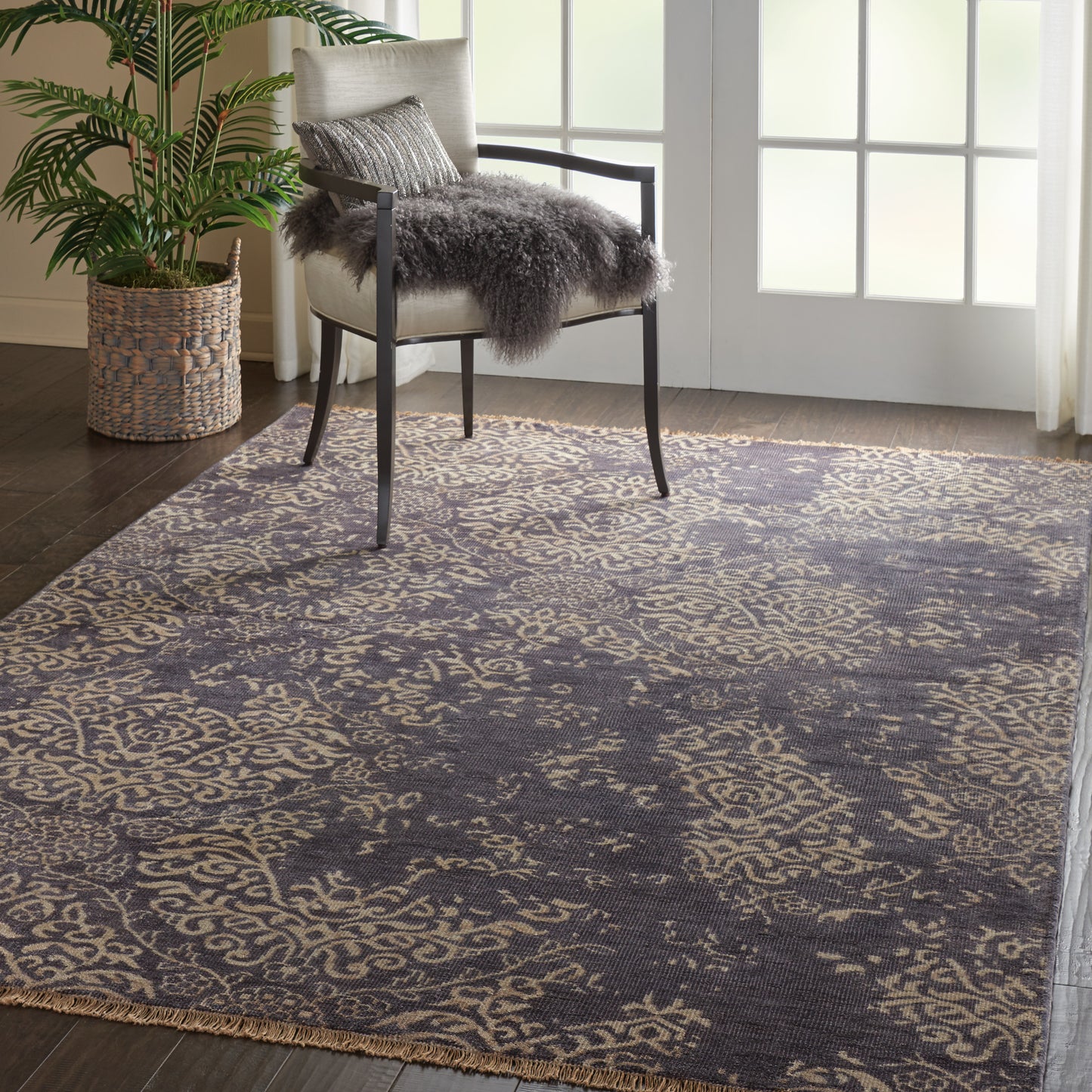 Ornate navy blue & beige area rug with scroll pattern in a living room, paired with a chair and sheepskin throw.